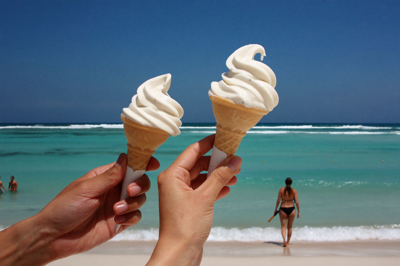 Two soft-serve cones held up against the turquoise Sunshine Coast ocean